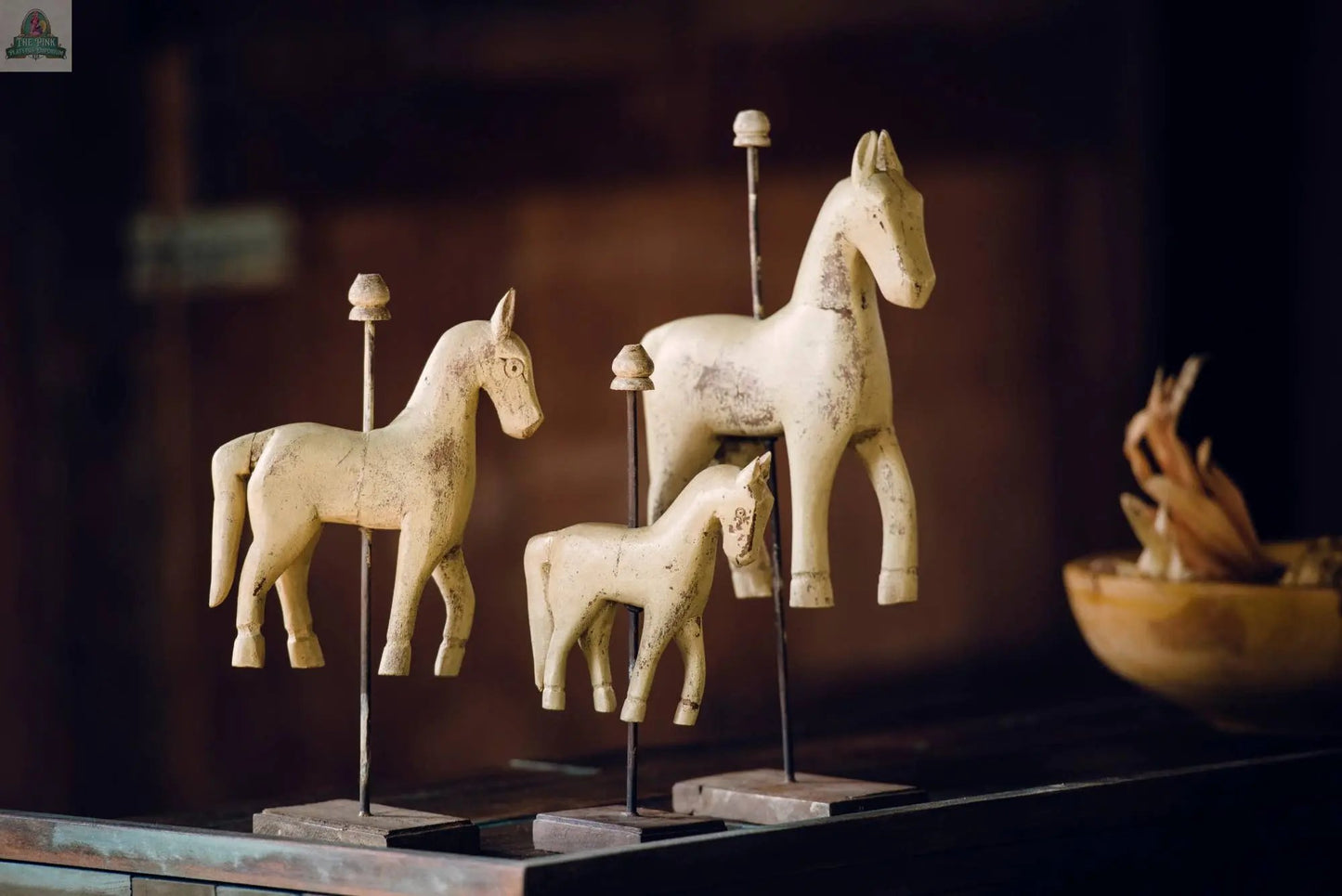 Three Carousel Horse Solid Wood Vintage Rustic Ocean Green 10" figurines, each on a vertical metal stand, are displayed on a dark wooden surface with a blurred brown background and a bowl to the right—ideal for rustic décor.