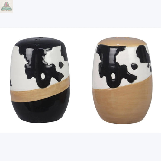 The Young's Ceramic Country Salt Pepper Shaker Set features two cow print shakers, each with a unique black, white, and tan pattern—one mostly black and the other with more tan on the lower half—perfect for farmhouse kitchen decor.