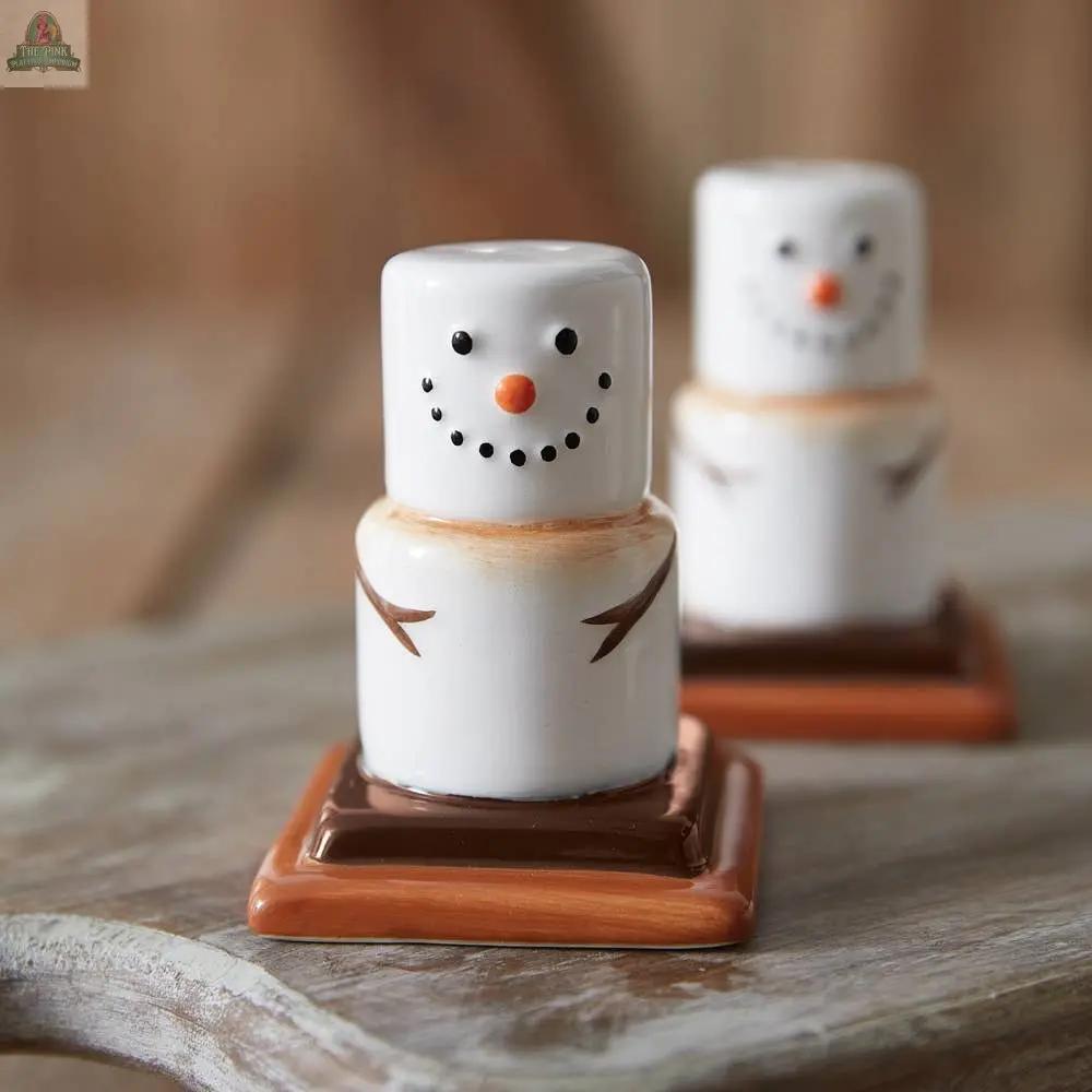 The Ceramic Smores Salt and Pepper Shakers feature cute snowmen with orange noses and twig arms on brown square bases, adding a whimsical touch to your dining table, especially when placed on a wooden surface.