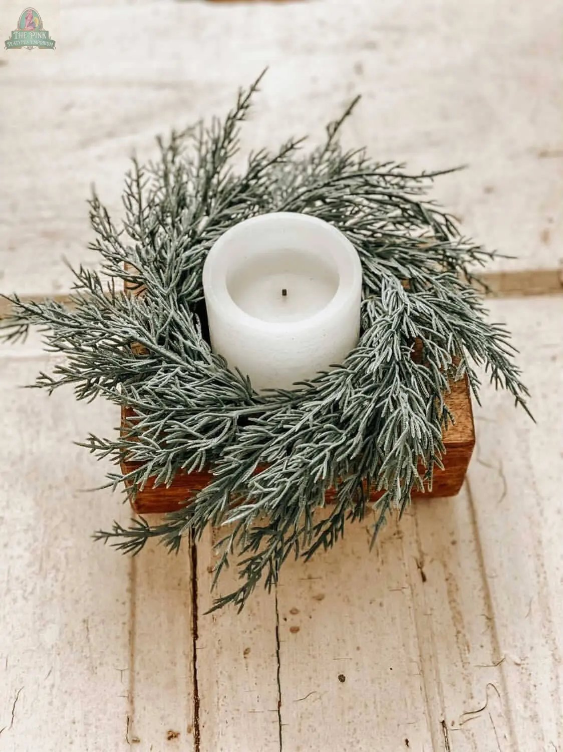 A white pillar candle rests in the Cheese Mold - 1 Hole, Candle Pour Ready, Handmade #A - 6.5, accented by artificial pine on a rustic wooden surface.