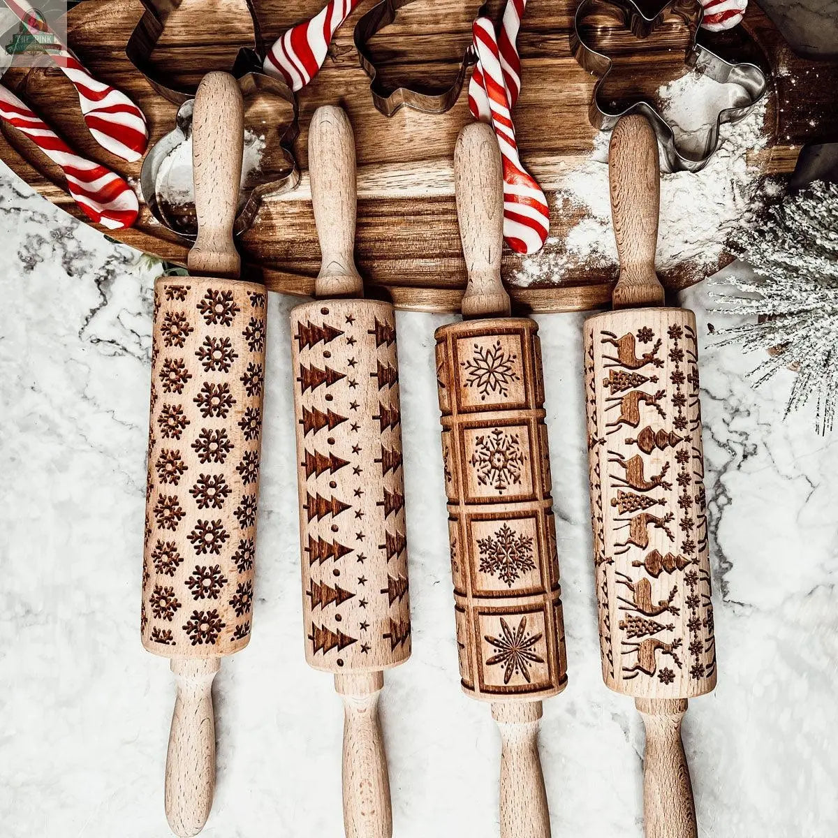 The Christmas Rolling Pin Set | 10 Styles is displayed on a marble surface with cookie cutters and holiday baking essentials, showcasing engraved festive patterns like snowflakes, Christmas trees, stars, and reindeer.