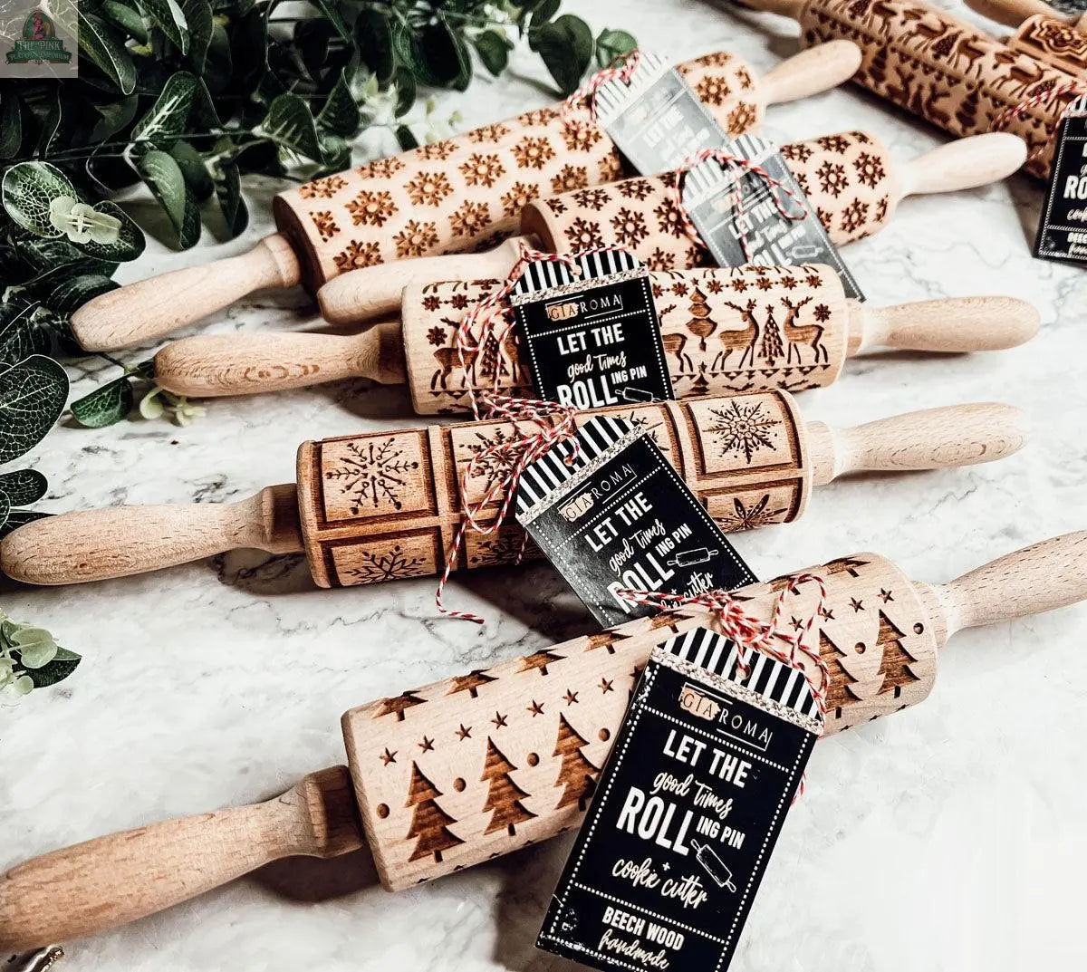 The Christmas Rolling Pin Set | 10 Styles features engraved wooden pins with festive designs like snowflakes, reindeer, and trees—each with a tag and red-and-white string. Perfect for holiday baking and beautifully displayed on marble with greenery.
