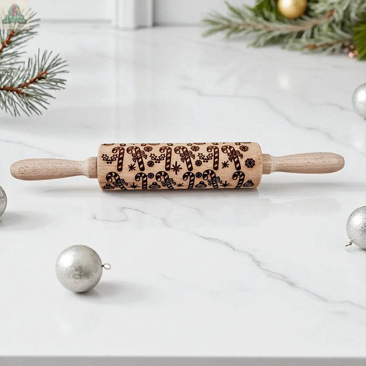 The Christmas Rolling Pin Set | 10 Styles, featuring engraved holiday patterns, is ideal for festive baking and is pictured on a white marble surface accented with pine branches and silver ornaments.