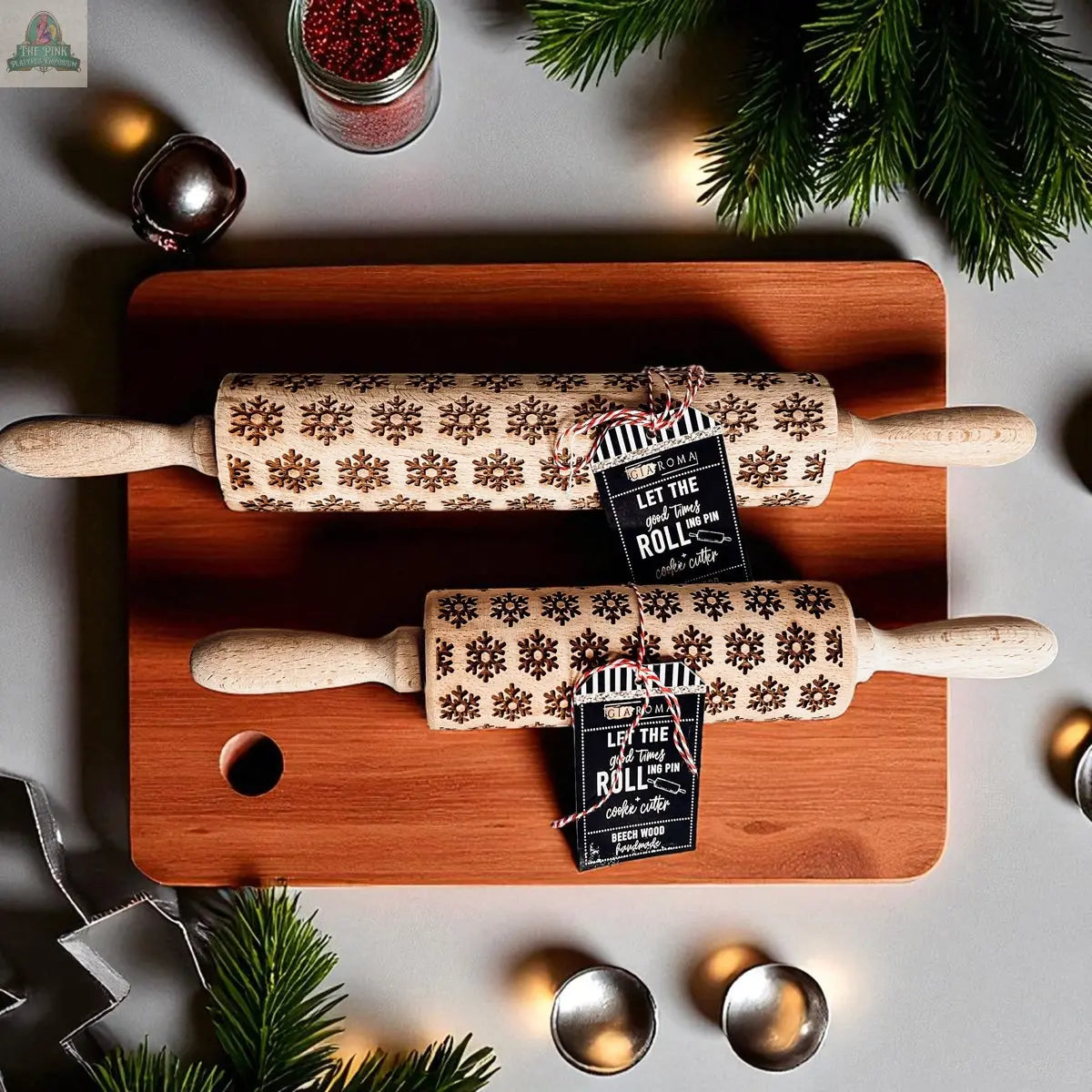 The Christmas Rolling Pin Set | 10 Styles features engraved rolling pins on a cutting board, ideal for holiday baking. Each has festive tags and is surrounded by greenery, bells, and cookie cutters for a cheerful holiday touch.