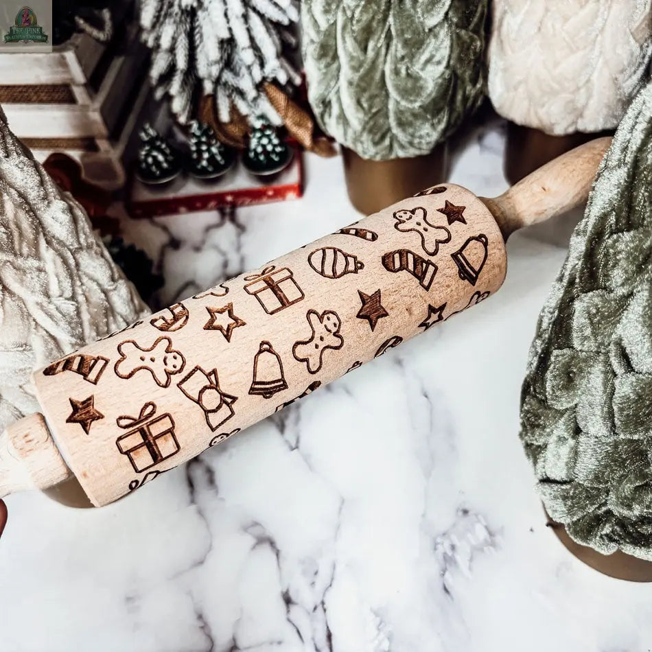 The Christmas Rolling Pin Set | 10 Styles features wooden pins engraved with festive designs and is displayed among plush green and white Christmas trees on marble—a charming gift for bakers this holiday season.