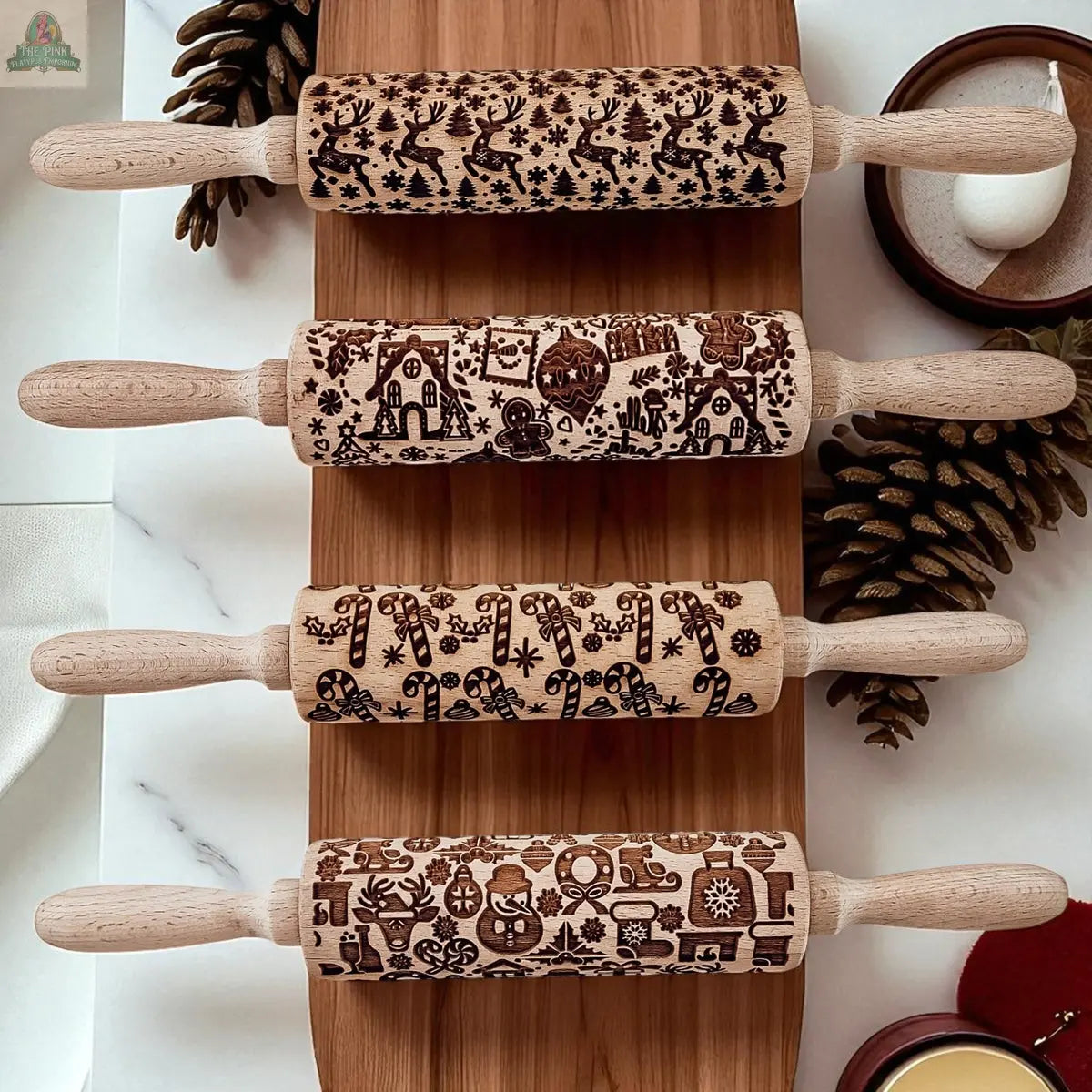 The Christmas Rolling Pin Set | 10 Styles features engraved festive designs like reindeer, gingerbread houses, Christmas trees, and ornaments, displayed with matching cookie cutters amid pinecones and holiday decor.