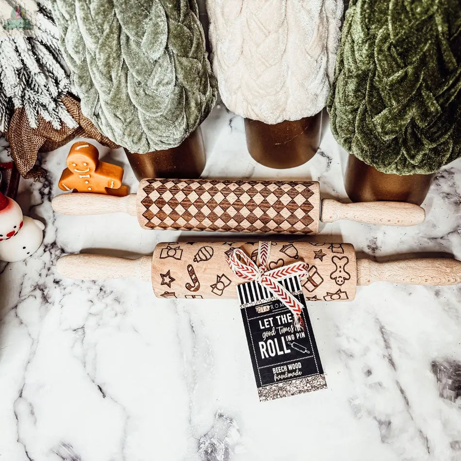 The Christmas Rolling Pin Set | 10 Styles features two wooden pins—one diamond-patterned, one with festive designs—displayed on marble next to velvet Christmas trees. A red and white string-tied tag hangs from the lower rolling pin.