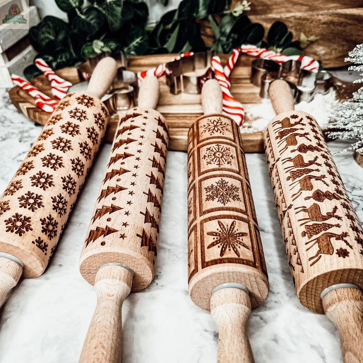 The Christmas Rolling Pin Set | 10 Styles features engraved holiday patterns, displayed with candy canes and greenery on marble—an ideal gift for bakers to use with cookie cutters this festive season.