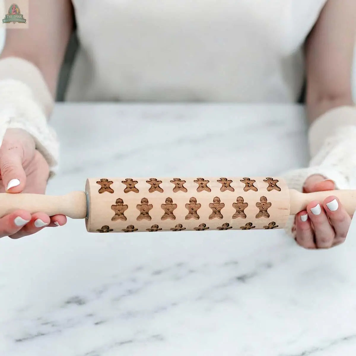 A person holds a Christmas Rolling Pin Set | 10 Styles, featuring engraved gingerbread men—ideal for holiday baking—over a white marble surface.