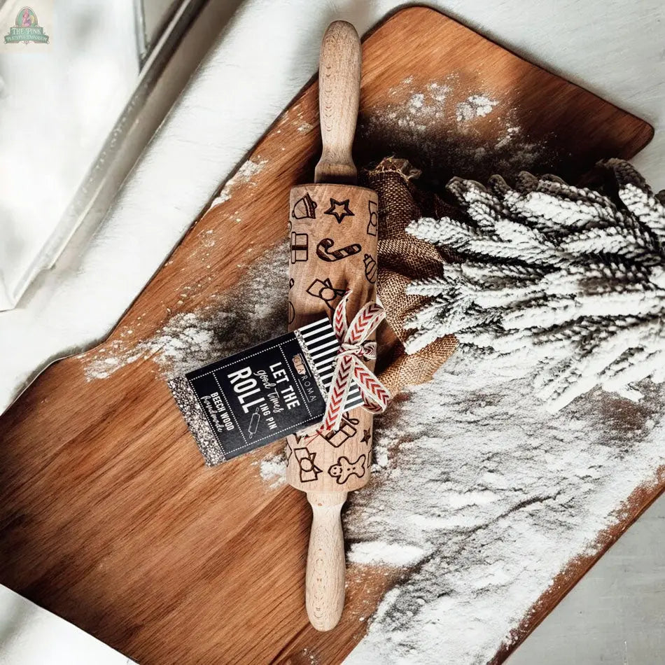The Christmas Rolling Pin Set | 10 Styles, featuring festive patterns, rests on a floured wooden board with pine branches, cookie cutters, and a tag reading LET THE TIME ROLL.