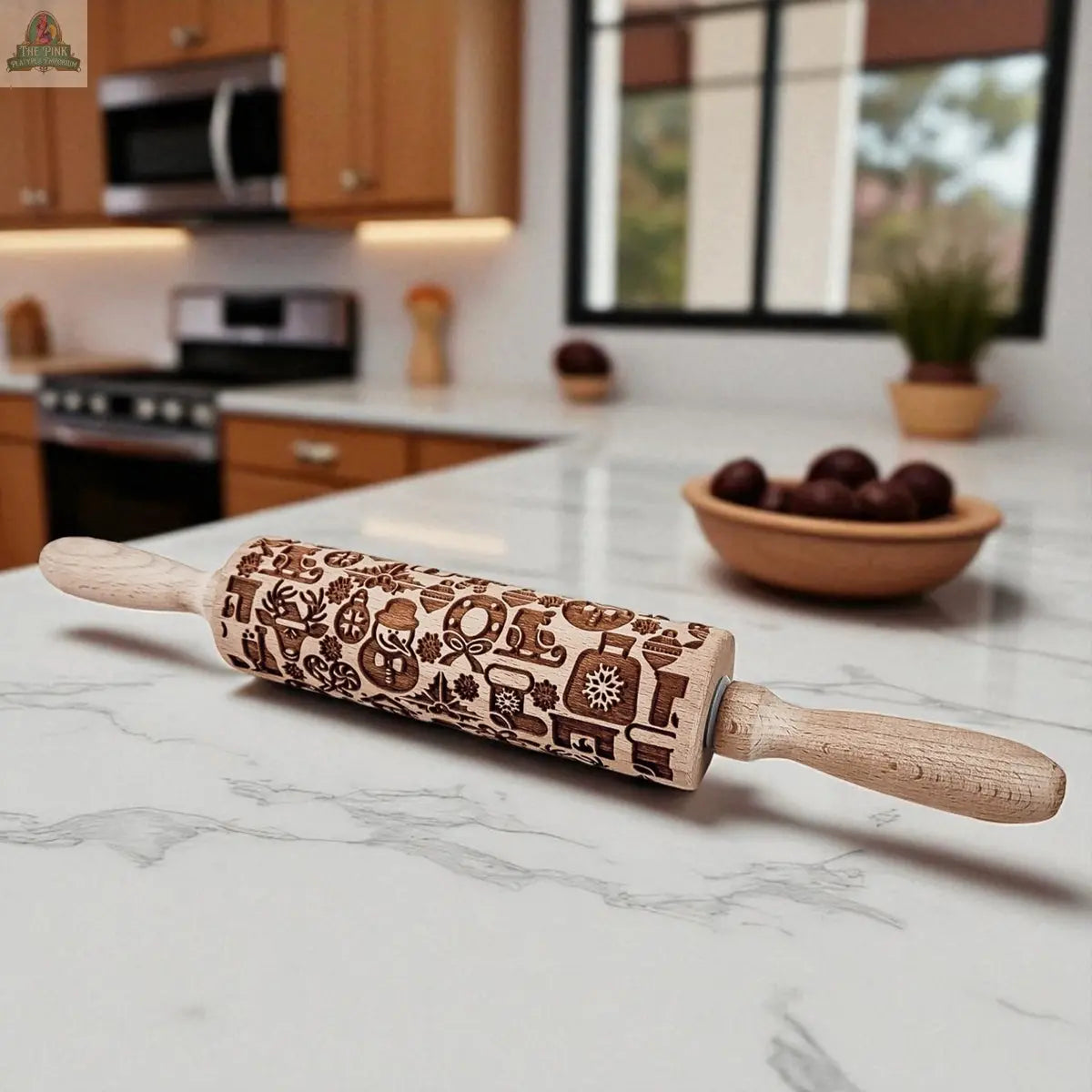 The Christmas Rolling Pin Set | 10 Styles, featuring engraved patterns, rests on a marble countertop—an ideal baking gift. A bowl of dark red fruits and a modern kitchen with light wood cabinets can be seen in the background.