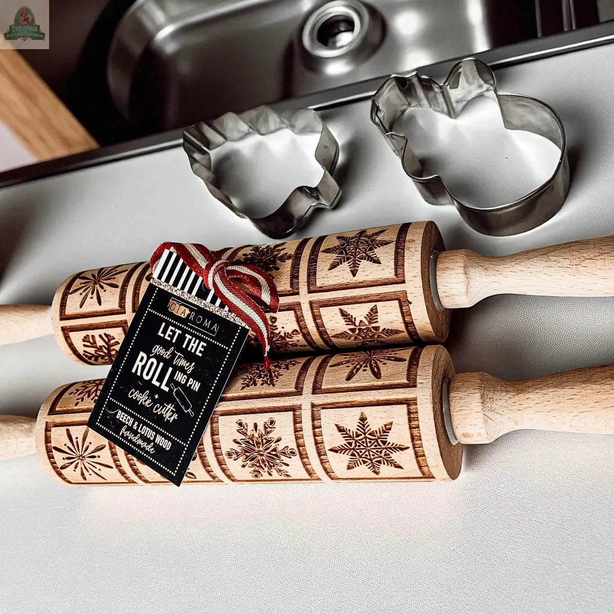 The Christmas Rolling Pin Set | 10 Styles includes two wooden snowflake pattern rolling pins, a festive tag, and metal reindeer and tree cookie cutters, making a charming baking gift on a white countertop by the kitchen sink.