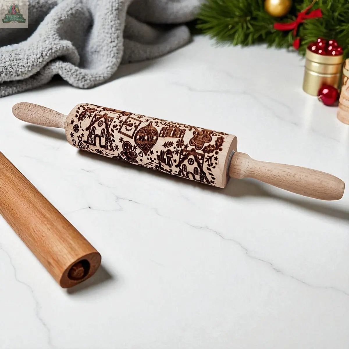 The Christmas Rolling Pin Set | 10 Styles, ideal as a baking gift, rests on a marble countertop beside a plain rolling pin, cookie cutters, a towel, and festive Christmas decor.