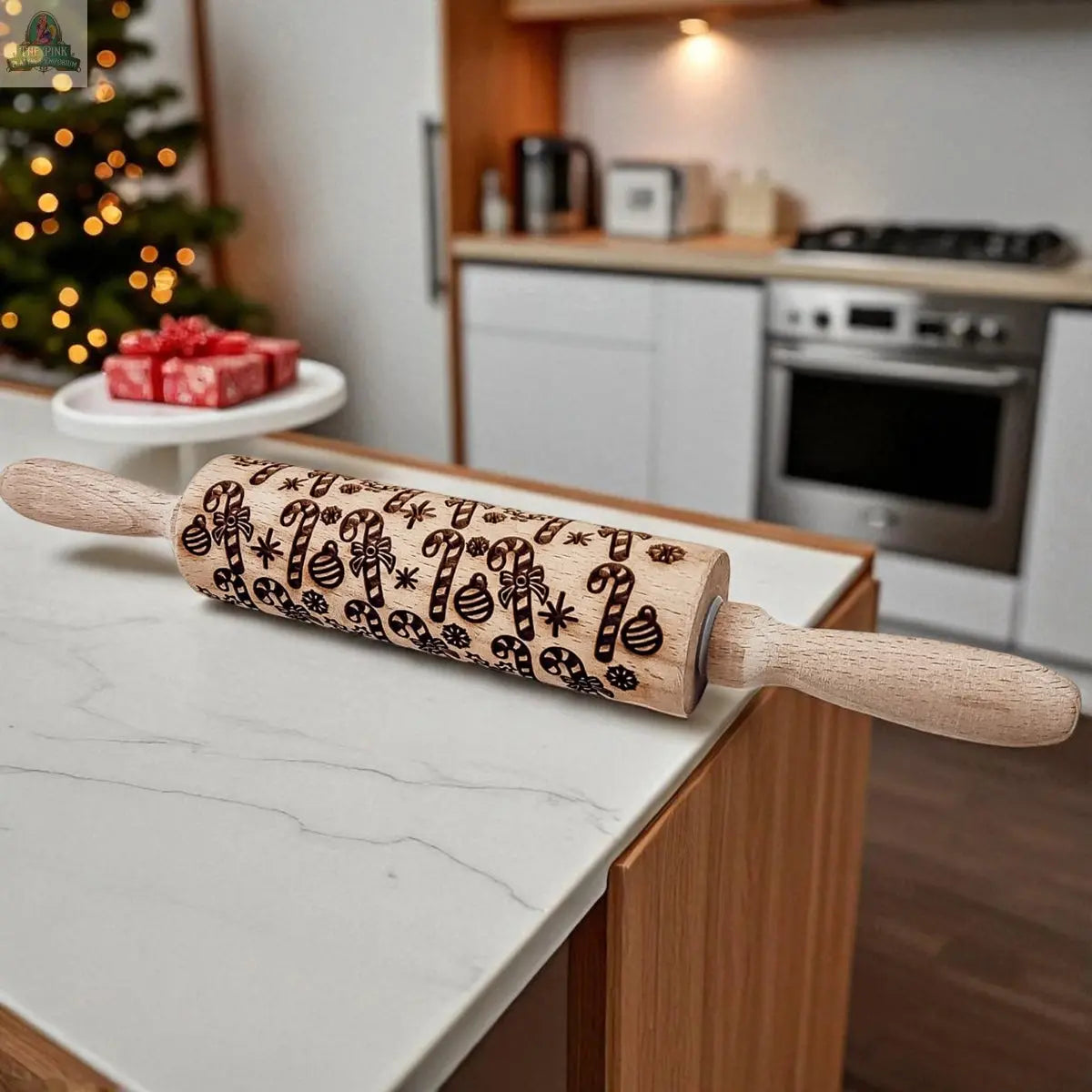 The Christmas Rolling Pin Set | 10 Styles, featuring festive patterns like candy canes and snowflakes, is on a kitchen counter with cookie cutters. A Christmas tree and gifts in the background add holiday cheer.