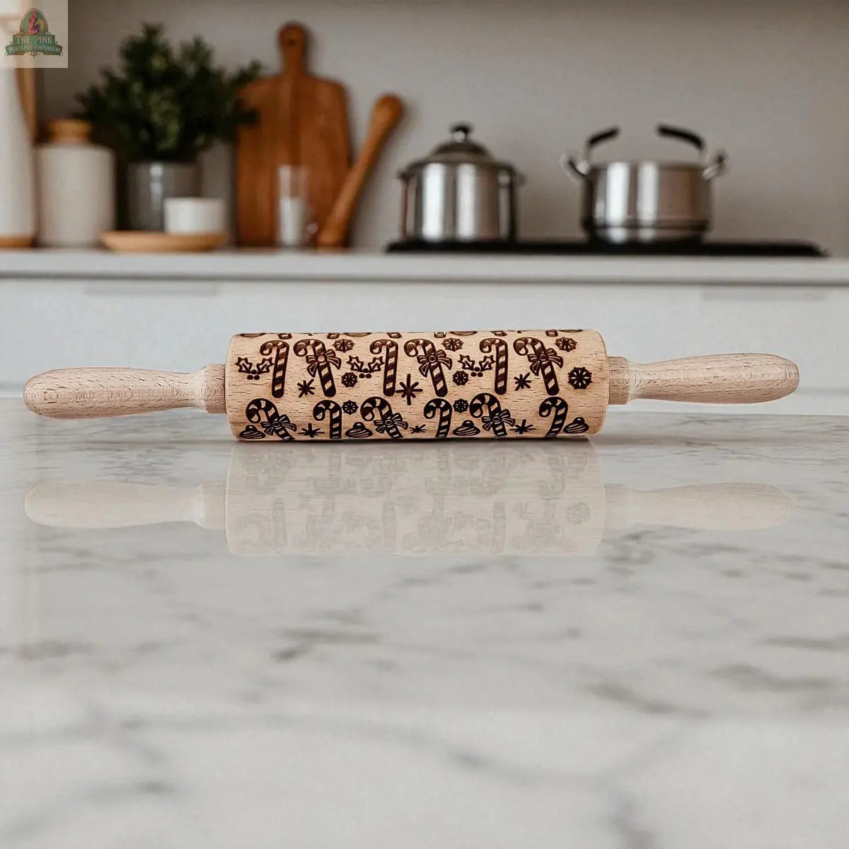 The Christmas Rolling Pin Set | 10 Styles, engraved with festive designs, sits on a marble countertop—perfect for holiday baking gifts—in a modern kitchen featuring pots, cookie cutters, and cutting boards in the background.