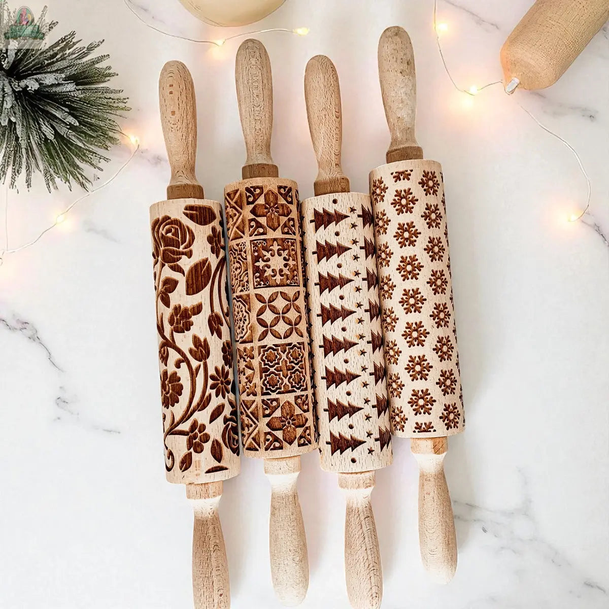 The Christmas Rolling Pin Set | 10 Styles features engraved pins in festive patterns, displayed on a white marble surface with holiday lights and a pine branch—perfect as a unique baking gift for any enthusiast.