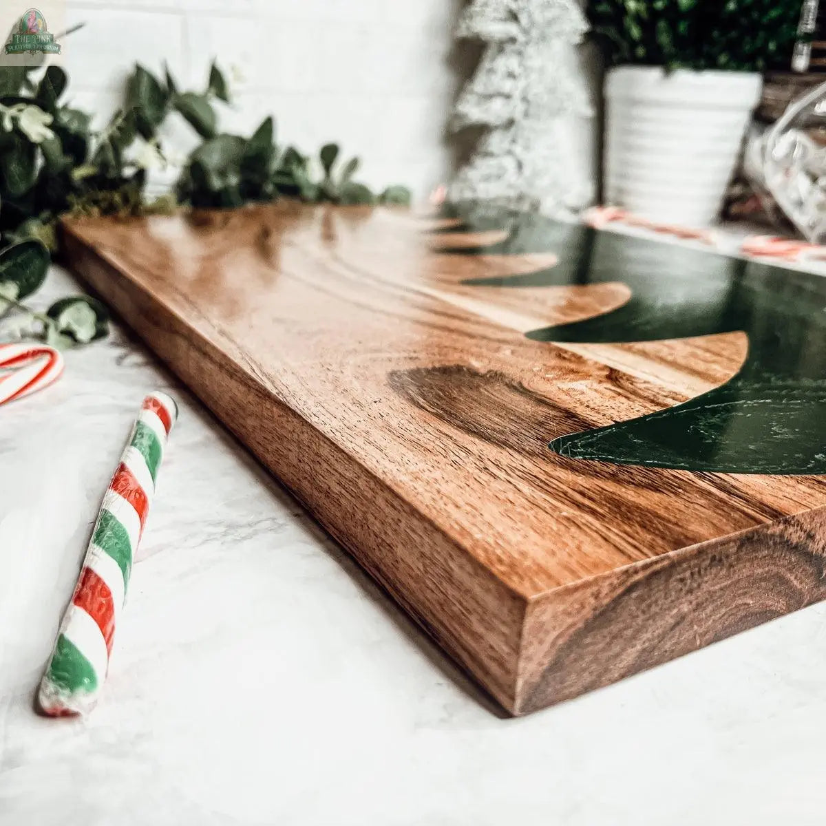 A close-up of the Christmas Serving Board, hand-crafted with a green painted Christmas tree design, displayed beside a green, red, and white striped candy cane and festive greenery.