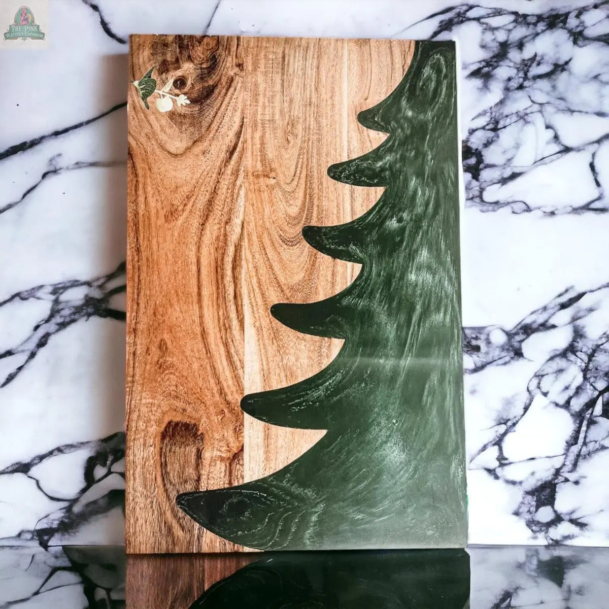 The Christmas Serving Board is a hand-crafted wooden charcuterie board with a green painted Christmas tree silhouette on one side, shown on a white surface with black marble-style veins.