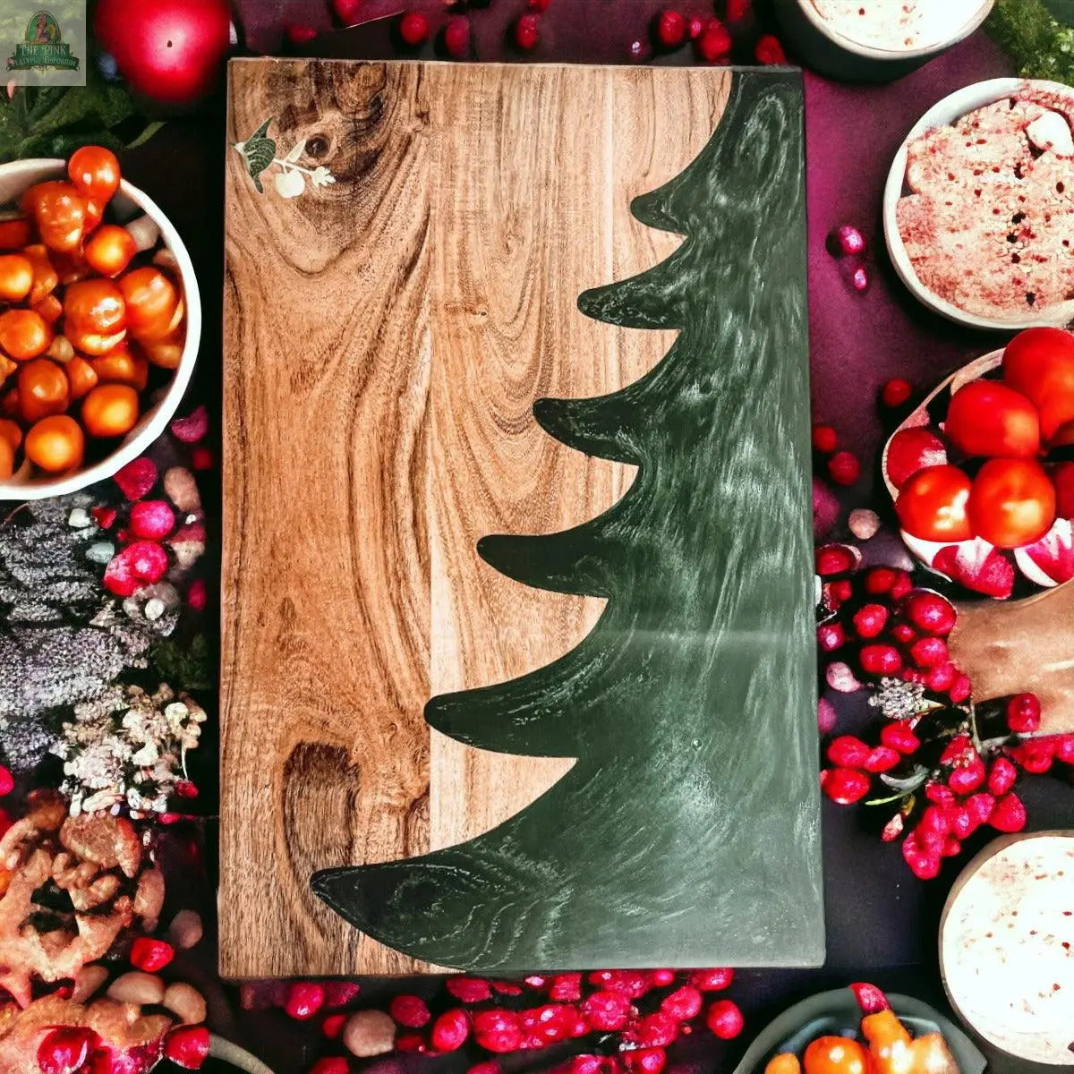 The Christmas Serving Board, hand-crafted with a Christmas tree design, is surrounded by bowls of cherry tomatoes, berries, bread, and festive treats on a dark surface.