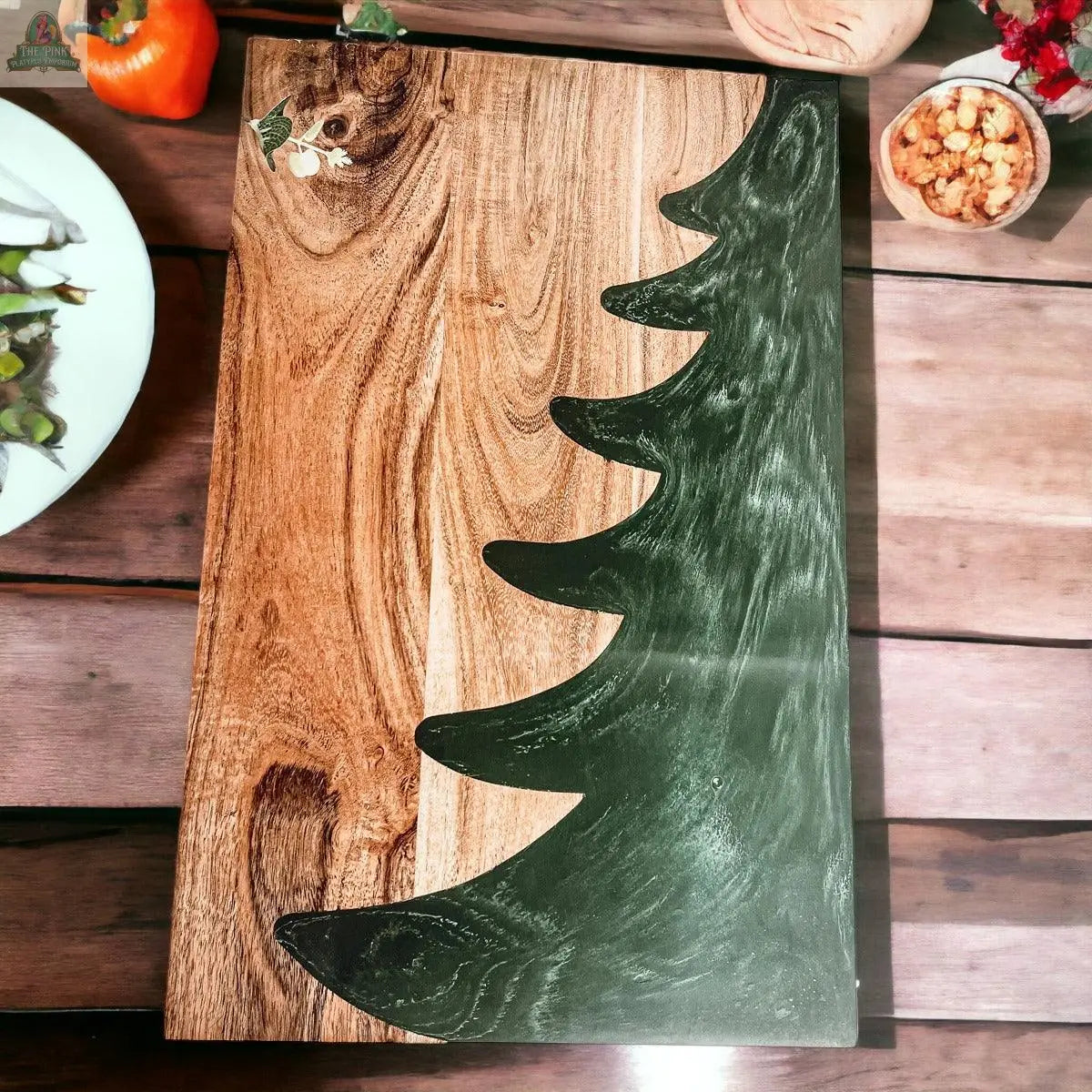 The Christmas Serving Board is a hand-crafted rectangular wooden board with a painted green Christmas tree design, perfect for serving snacks and festive treats.