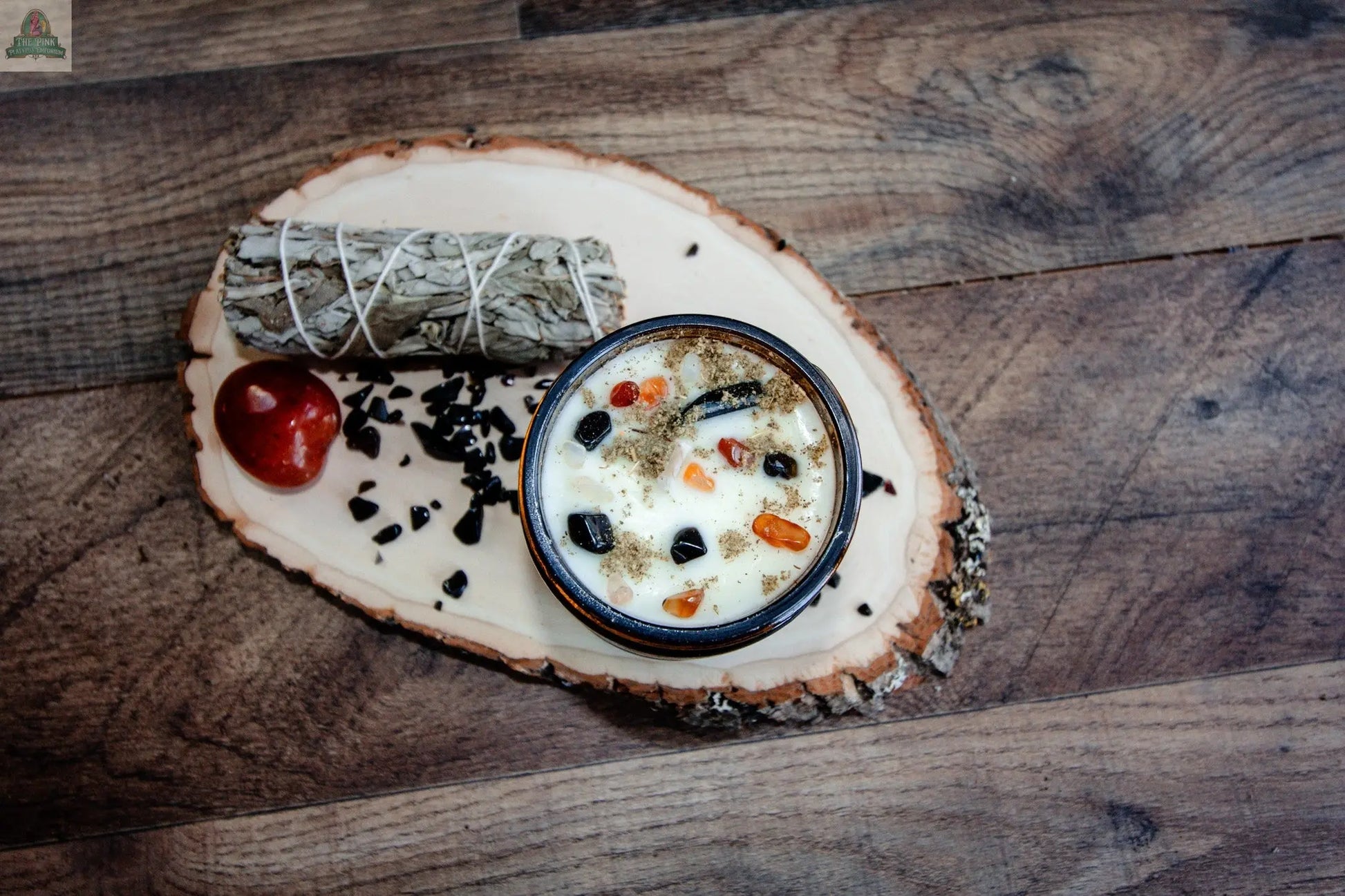 A cup of Cleansing creamy vegetable soup rests on a wooden slice, with sage, a crystal energy candle, and a red stone—all displayed on a wood-grain surface.