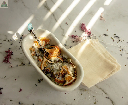 A white ceramic bowl holds Cleansing—a blend of dried orange slices, herbs, and salt—on a marble surface. Use this herbal bath tea with the included sachet bags to elevate your self-care routine with scattered dried herbs and flowers.