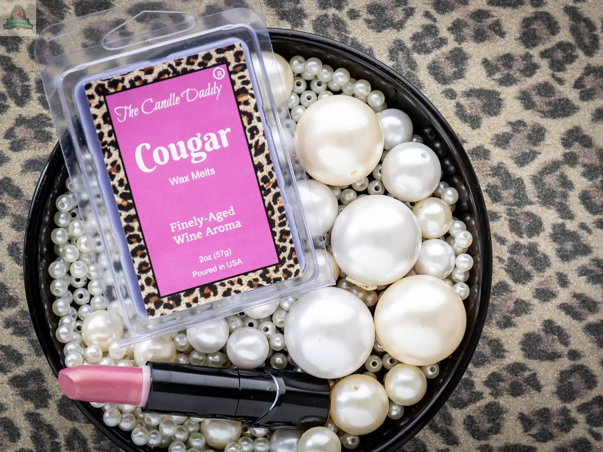 A 2-ounce pack of Cougar - Fine Wine Scented Wax Melts Cubes with a leopard print border rests on assorted pearls beside a pink lipstick, all displayed on a leopard print surface.