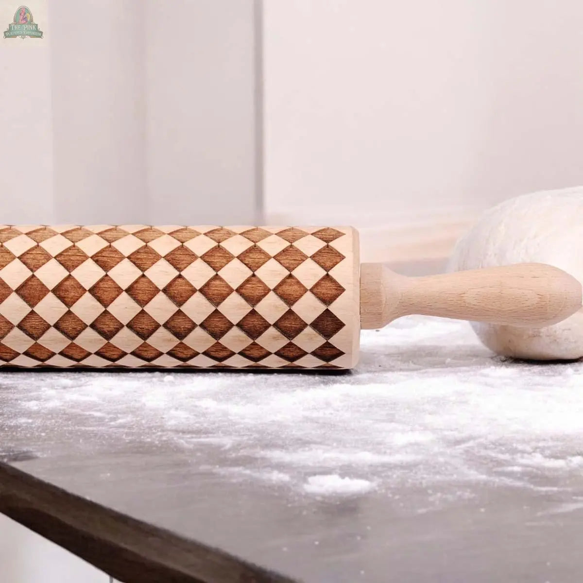 The Courtly Check patterned wooden rolling pin, featuring a diamond design, rests on a floured surface beside dough—ideal for baking enthusiasts.