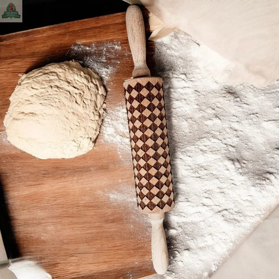 A Courtly Check rolling pin rests on a floured wooden surface beside a ball of dough, with flour scattered across the area and other essential baking tools nearby, ready for baking.