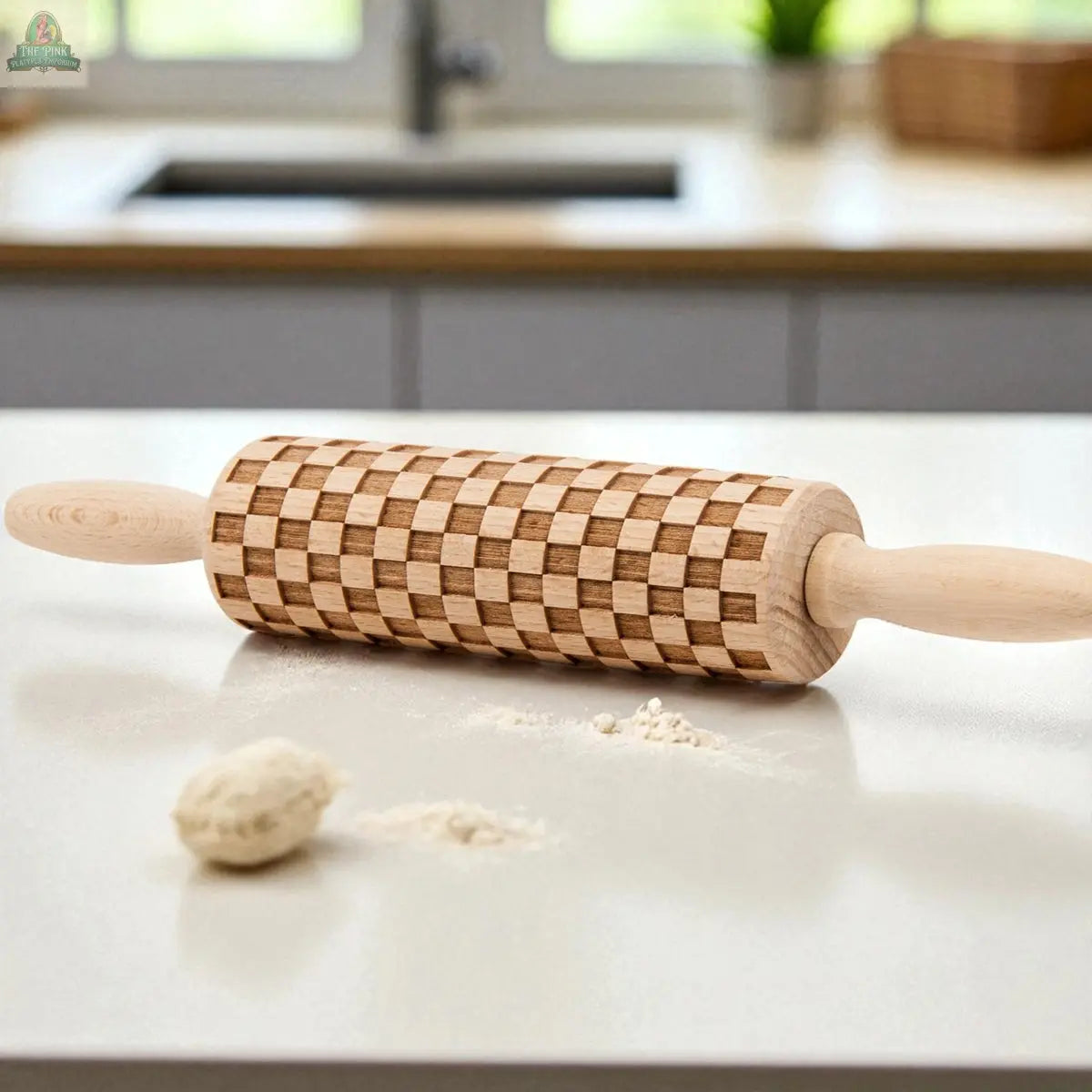 A Courtly Check rolling pin rests on a white kitchen counter beside cookie cutters, dough, and flour, with a sink and window in the background.