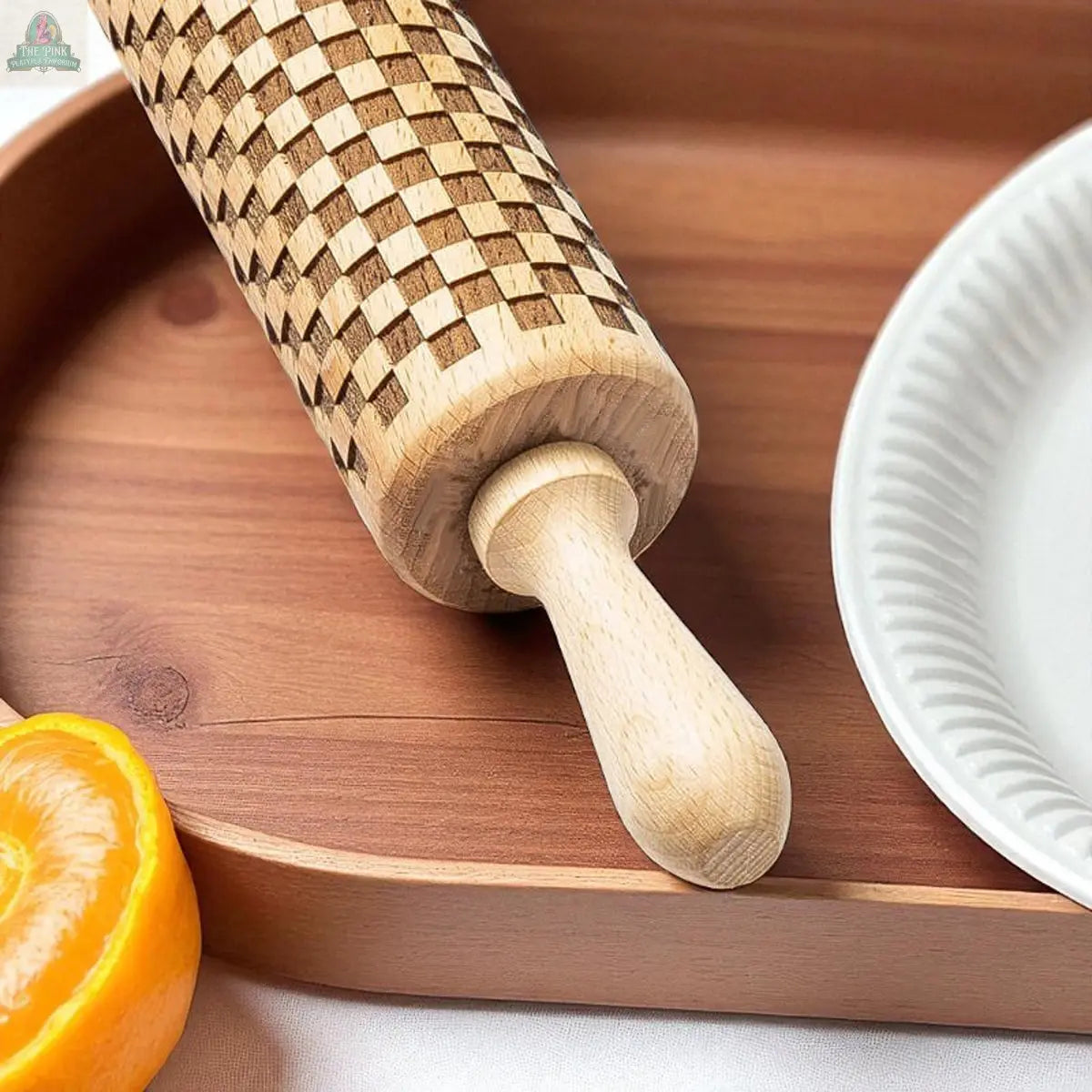 The Courtly Check Rolling Pin, featuring a classic checkered pattern, rests on a wooden tray beside a white plate and orange—an ideal addition to your Courtly Check baking collection.