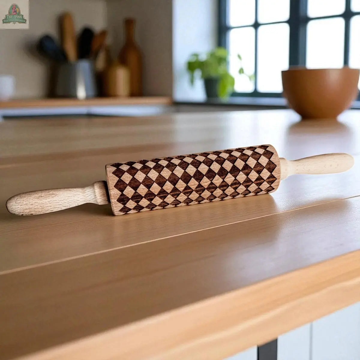 The Courtly Check rolling pin, featuring a geometric diamond pattern, sits on a wooden kitchen counter amid baking tools, cookie cutters, utensils, a bowl, and a potted plant in the background.