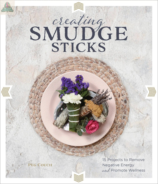 A pink plate with assorted flowers and herbs for smudge sticks sits on a woven placemat beside the Creating Smudge Sticks Book by REDFeather, a perfect guide for crafting your own spiritual tools.