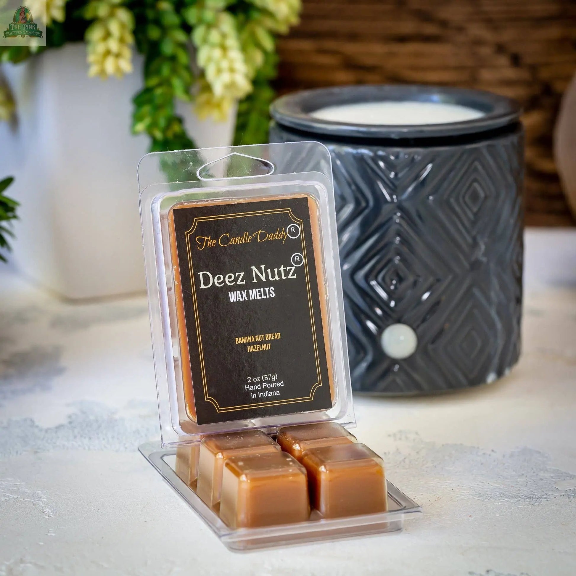 A pack of Deez Nutz Wax Melts - Banana Nut Bread sits on a white surface, with a black wax warmer and a plant in the background.