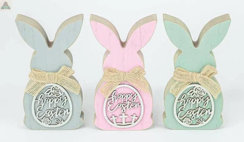 The Easter Egg Cutout Bunny Tabletop 3 Ast includes blue, pink, and green wooden bunnies (3.15x6.5x0.98 in) with bows, "Happy Easter" signs, and unique Easter-themed cutout accents on their backs.