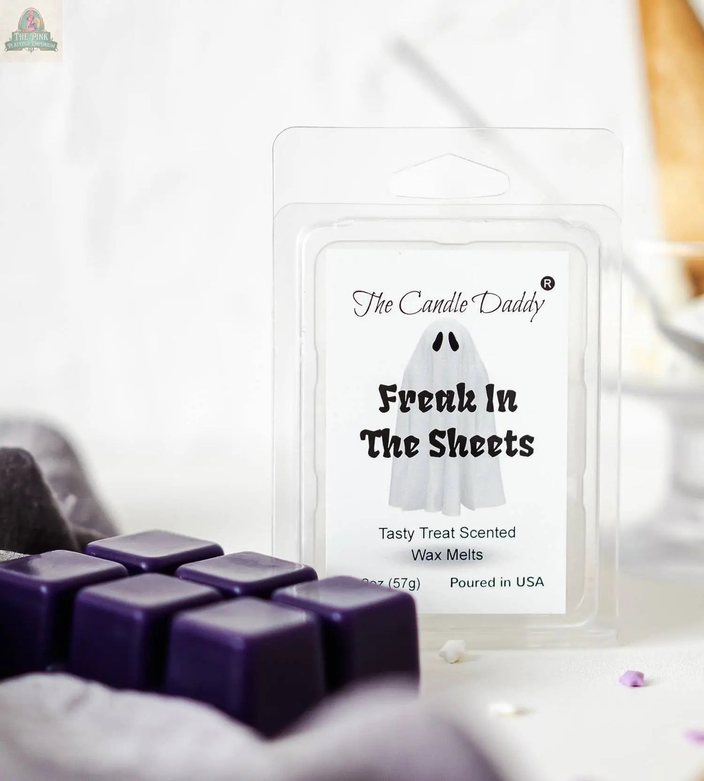 A package of FUNNY FALL HALLOWEEN - FREAK IN THE SHEETS - TREAT WAX MELT by The Candle Daddy, with a ghost design, sits beside purple wax cubes and is ideal for aromatherapy with its tasty treat scent.