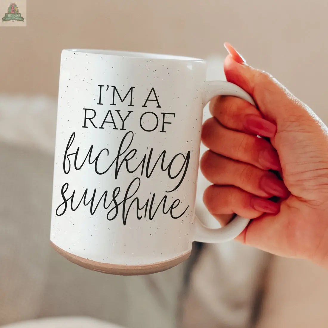 A hand with painted nails holds the F'n Sunshine 16oz ceramic mug, white and speckled, featuring bold script that reads "IM A RAY OF fucking sunshine.