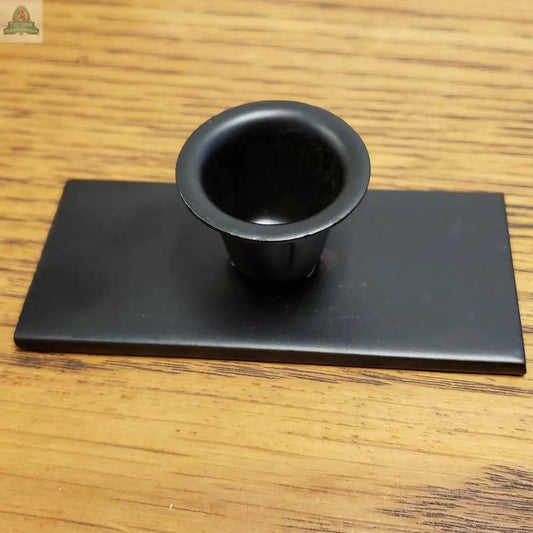 The Flat Base Taper Candle Holder, featuring a small black plastic cup with an elongated base, sits on a flat rectangular black stand and is displayed on a wooden surface.