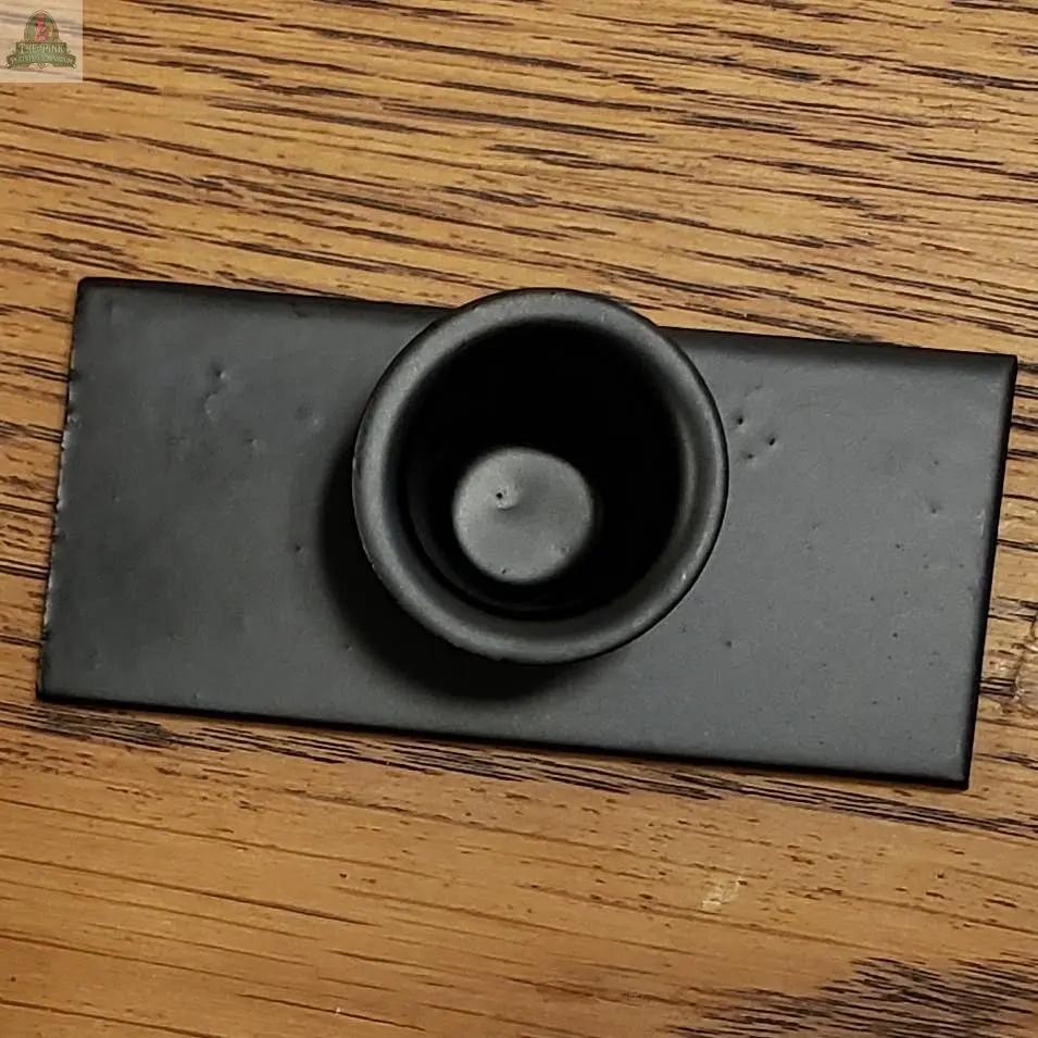 The Flat Base Taper Candle Holder, a small round black metal piece, rests on a rectangular black tray atop a wooden surface with visible grain.
