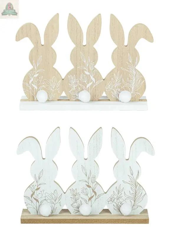 The Floral Bunny Trio Tabletop 2 Ast includes two sets of wooden bunny trios (11.5x1.97x8.27 in): one natural wood with white tails, the other white with wood bases and floral patterns—perfect for decorative displays.