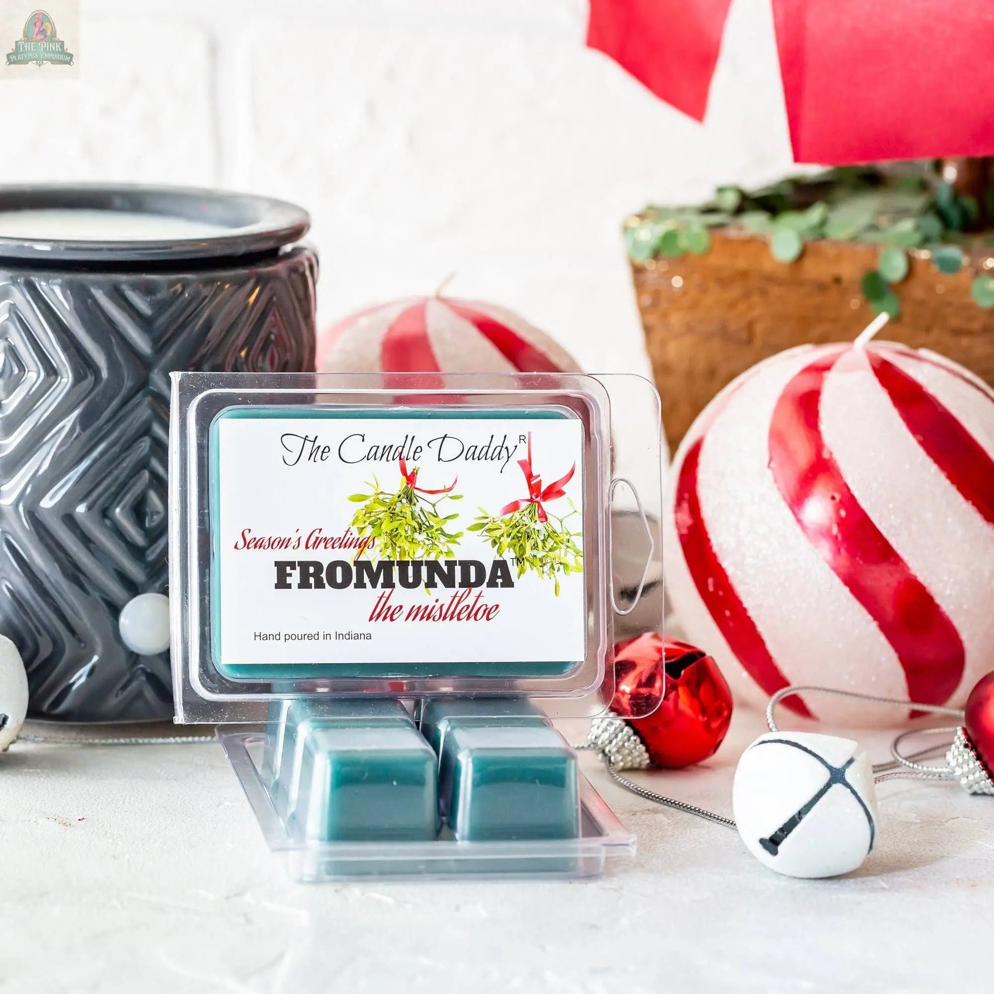 A black candle warmer with Fromunda The Mistletoe - Funny Christmas Under the Mistletoe: 1 Pack of Wax Melts, surrounded by red and white Christmas ornaments and jingle bells on a white surface.