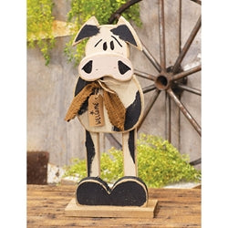 Decorative cow figurine with checkered pattern on a wooden stand, rustic background.