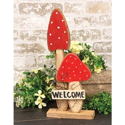 wooden mushroon welcome sign on a white brick background with greenery surrounding it