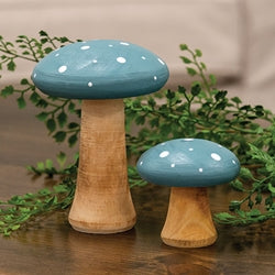 Two decorative mushroom figurines with blue caps and wooden bases on a reflective surface with greenery in the background.
