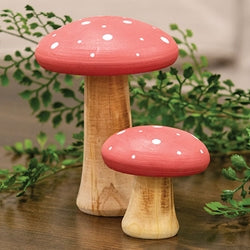 Two wooden mushroom-shaped figurines with red caps on a surface with greenery in the background.