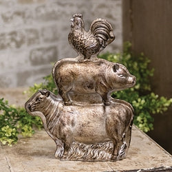 Decorative sculpture of animals stacked on top of each other with a rooster on top, set against a natural background.