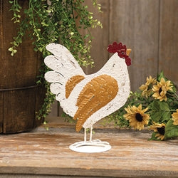 Decorative metal chicken sculpture on a wooden surface with plants in the background