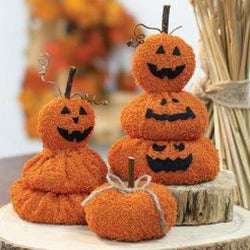 Decorative pumpkins made of yarn stacked on a wooden surface with a blurred background.