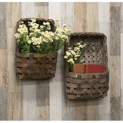 Two woven wall baskets with plants and books on a wooden wall.