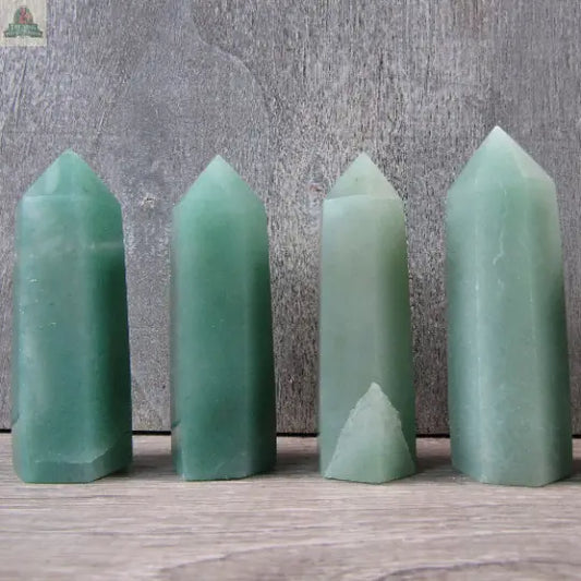 Four Keystone Crystals Gemstone Obelisks 2" Aventurine stand upright on a wooden surface against a rustic gray background—ideal healing crystals to enhance your space.